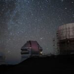 Un observatorio en el que hay varios edificios con telescopios que observa el espacio. En el fondo se aprecian las estrellas.