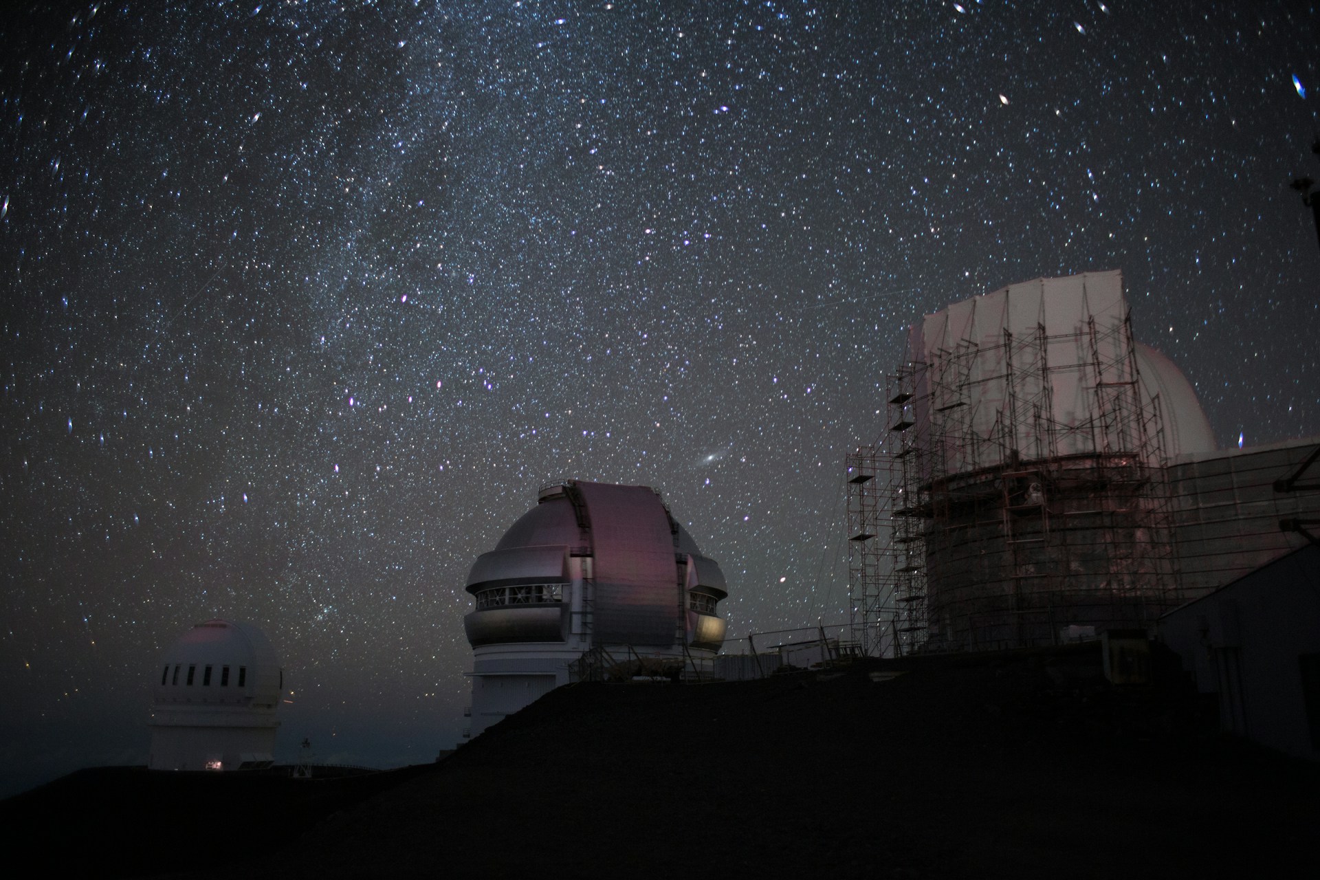 Un observatorio en el que hay varios edificios con telescopios que observa el espacio. En el fondo se aprecian las estrellas.