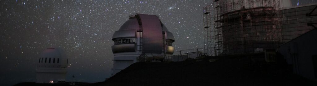 Un observatorio en el que hay varios edificios con telescopios que observa el espacio. En el fondo se aprecian las estrellas.