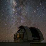 Un observatorio en el que hay un telescopio que observa el espacio. Se aprecian las estrellas, la vía láctea como galaxia y una estrella fugaz