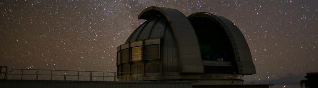 Un observatorio en el que hay un telescopio que observa el espacio. Se aprecian las estrellas, la vía láctea como galaxia y una estrella fugaz