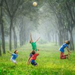 Cuatro niños saltando y lanzando una bola en la hierba verde