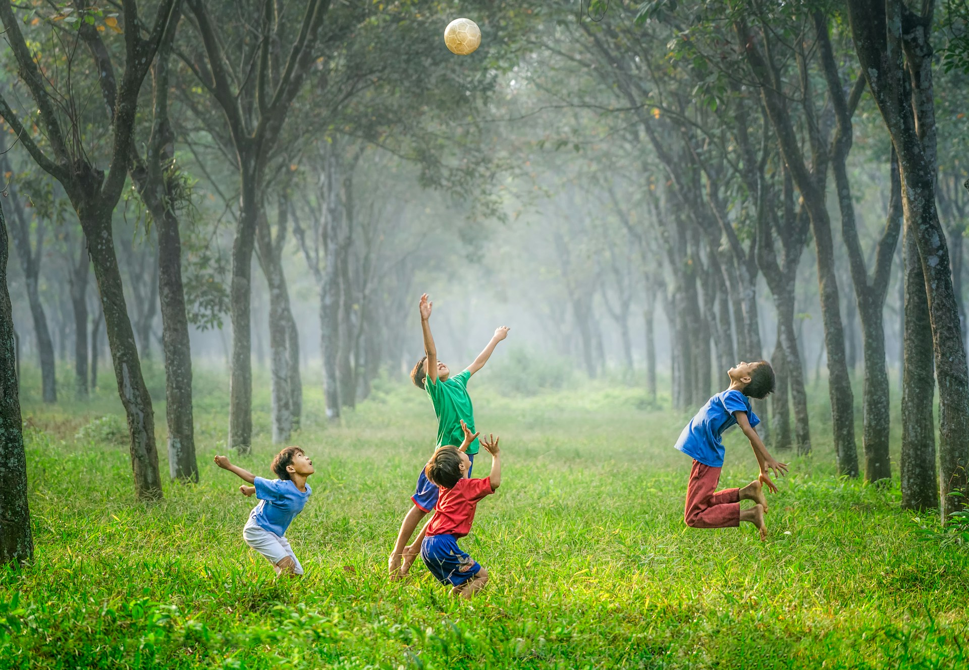 Cuatro niños saltando y lanzando una bola en la hierba verde