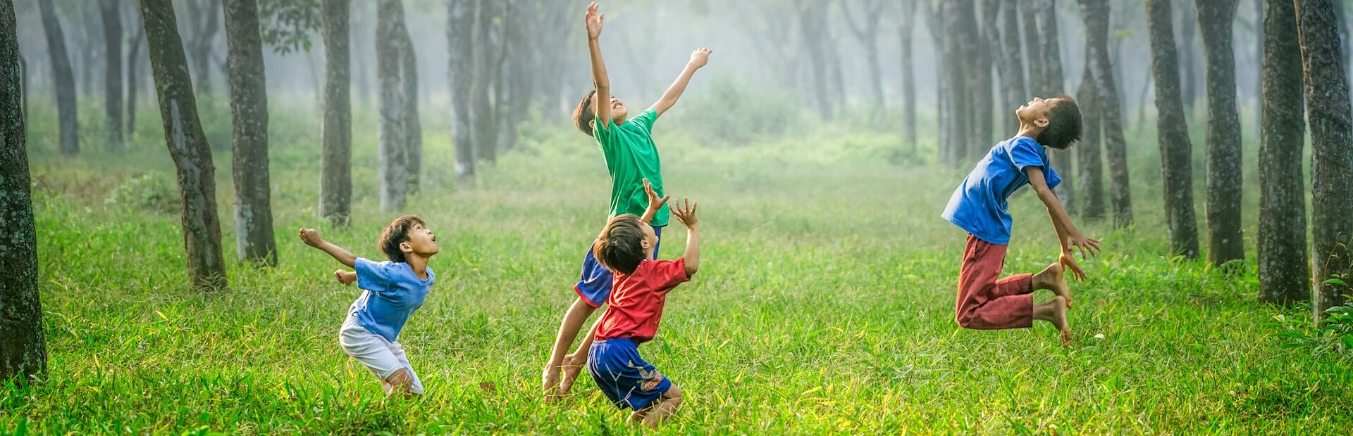 Cuatro niños saltando y lanzando una bola en la hierba verde