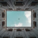 El cénit es el punto directamente sobre el observador. en la imagen se ve un avión en el cielo justo al pasar arriba de un área interior de un edificio con muchas ventanas.